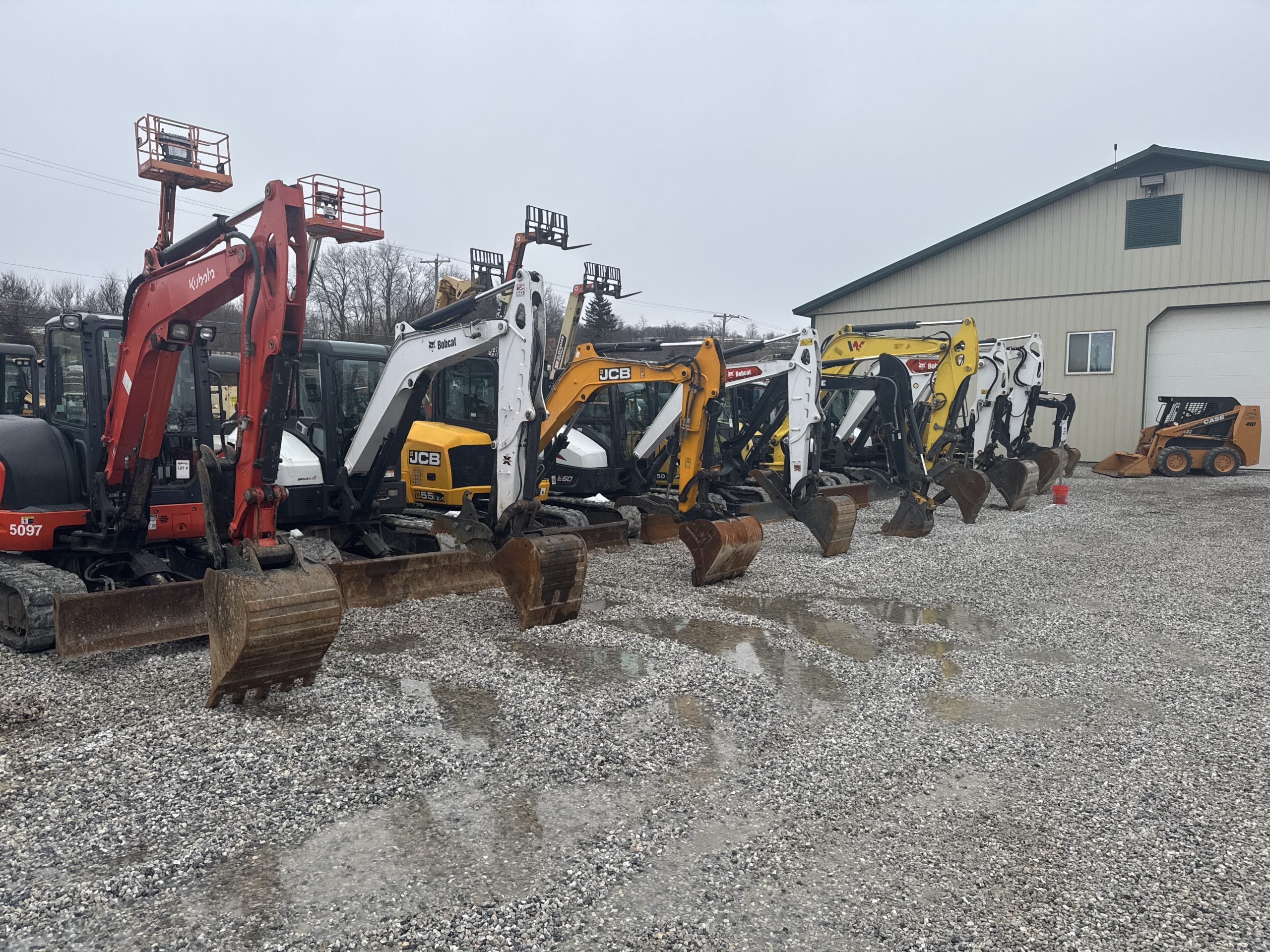 row of white and orange skid steer loaders parked on a gravel lot